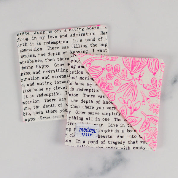 A corner bookmark with neon pink florals and black and white text laying on top of another one, backside up.